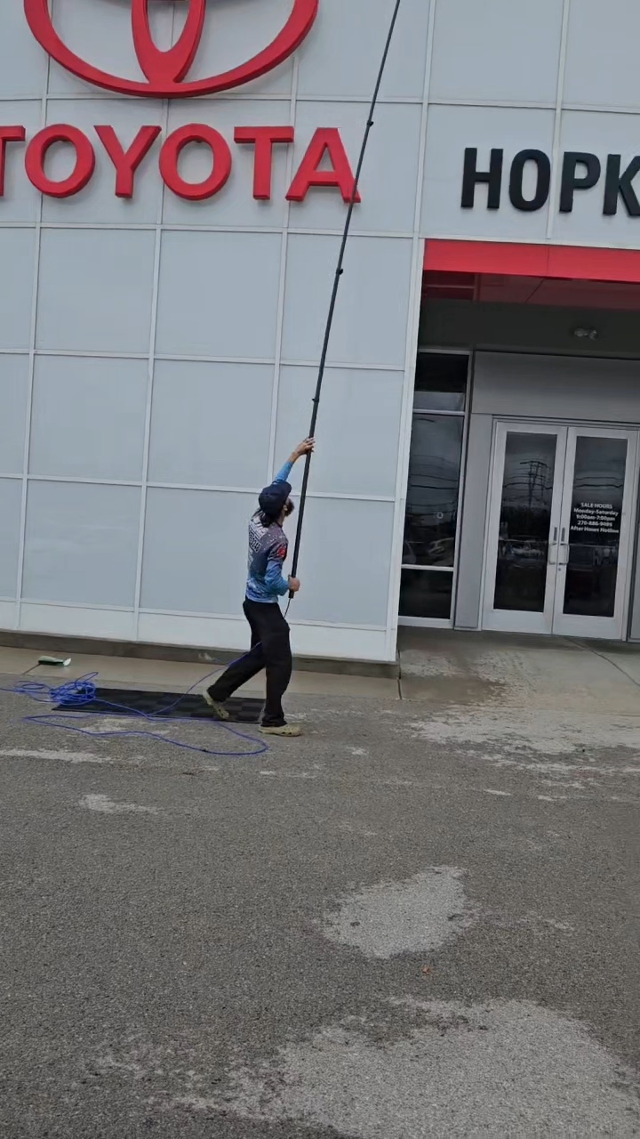 Hoyt's Pressure Washing technician cleaning a dealership storefront with an extension pole